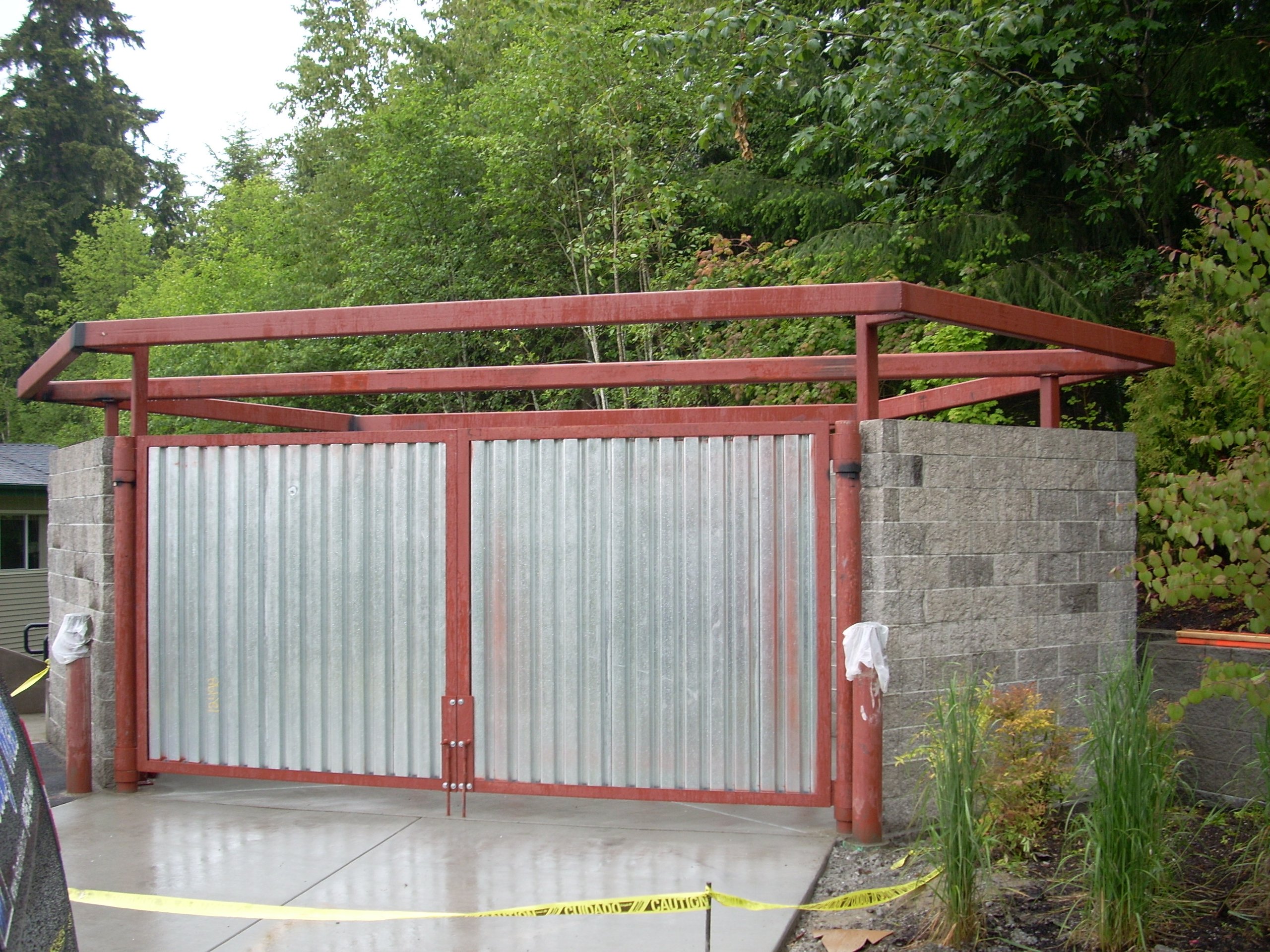 Red metal gate with corrugated panels between concrete walls near trees
