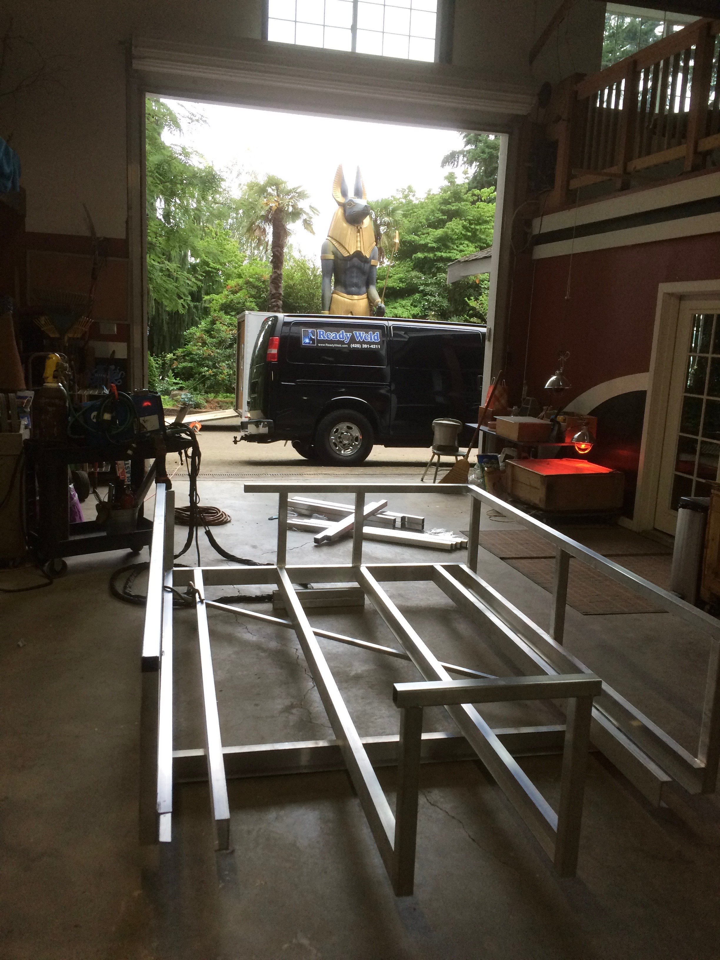 Workshop interior with metal frame, black van, and Egyptian statue outside