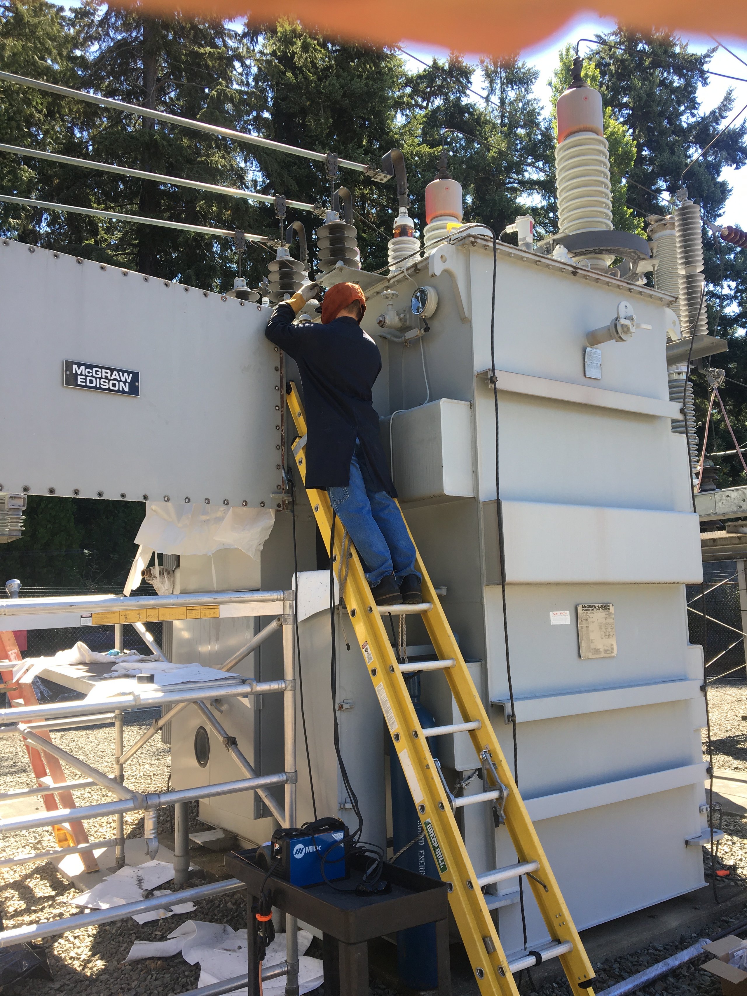 Technician on ladder repairing electrical transformer at McGraw Edison substation