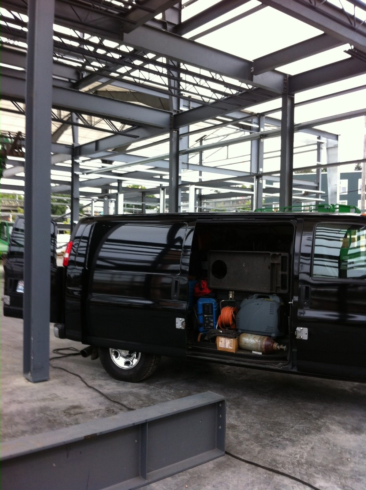 Black van with open side door revealing equipment in industrial garage