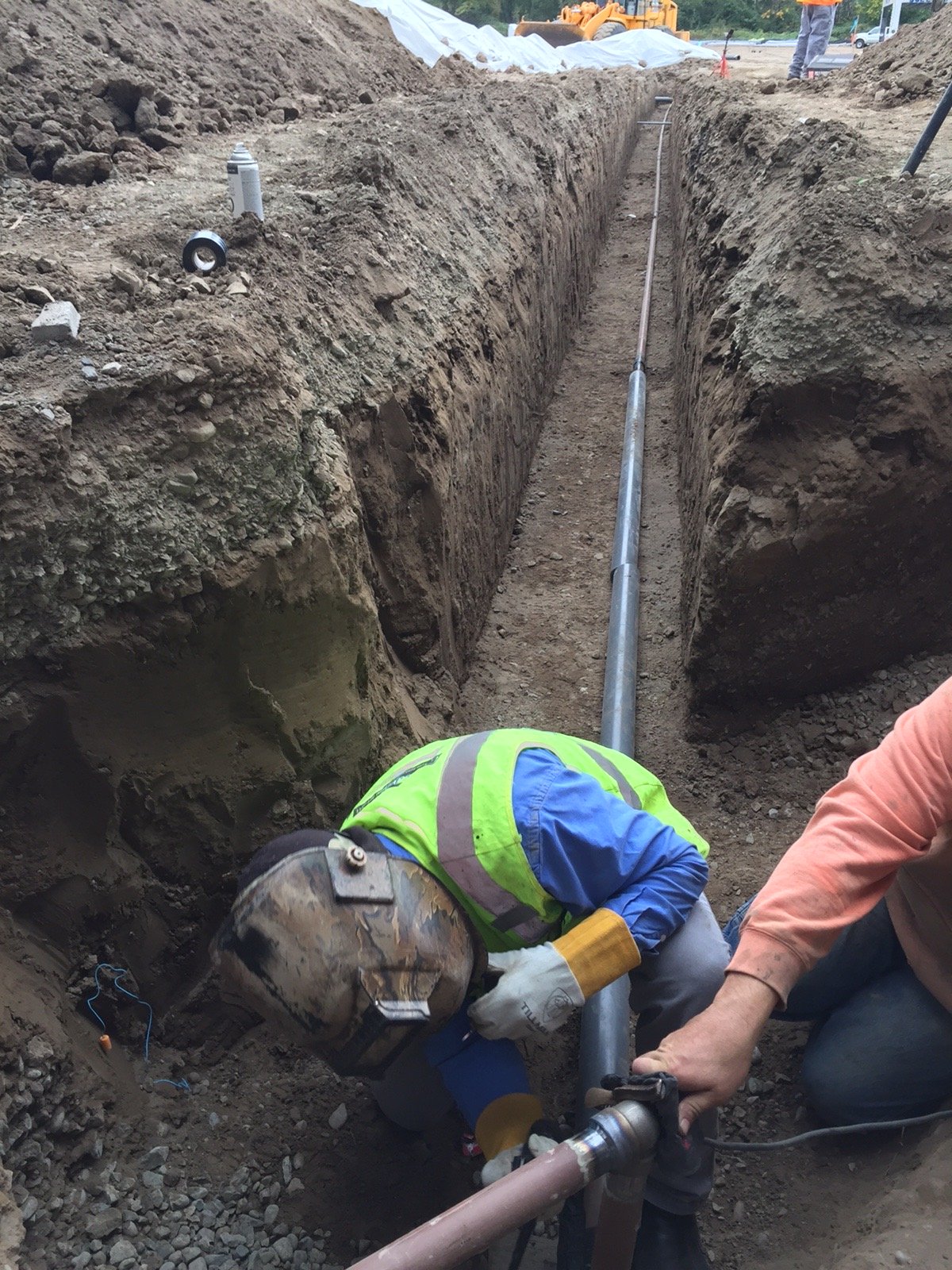 Construction workers installing underground pipe in deep trench